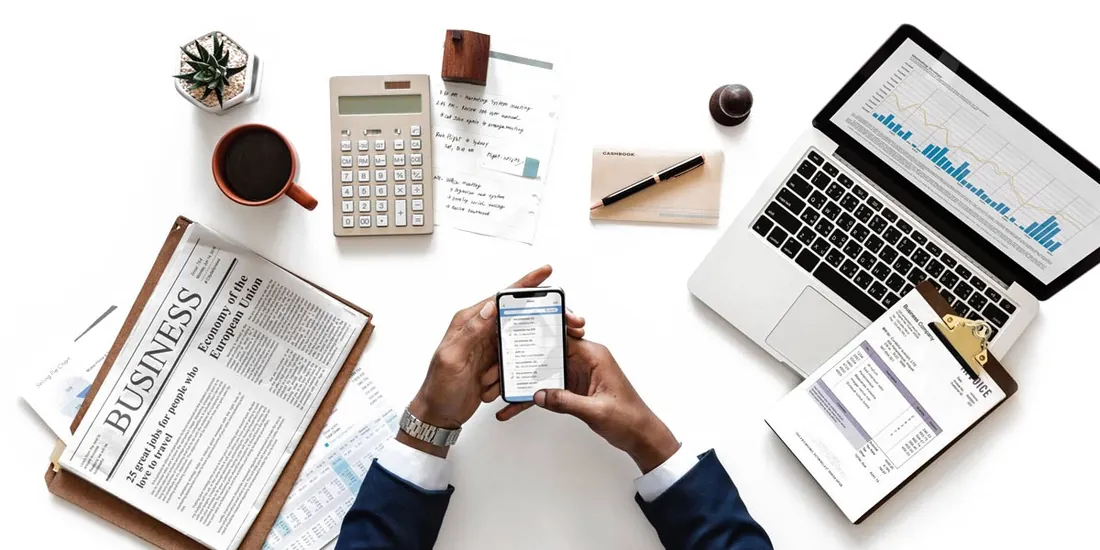 Business desk with laptop, charts and a person checking a phone