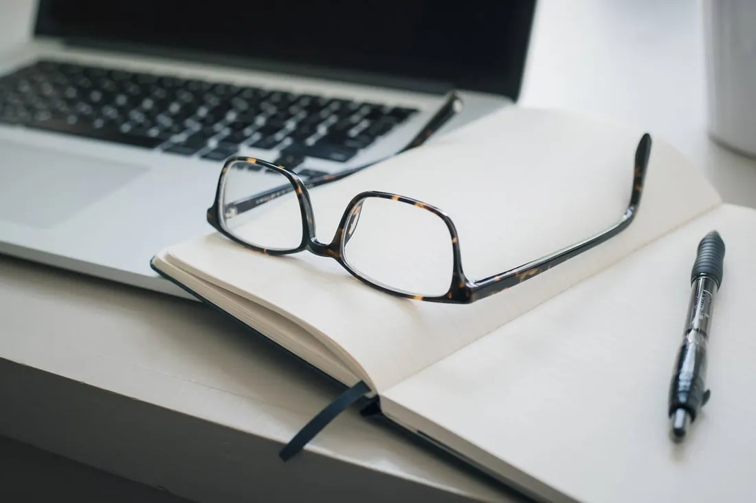 Eyeglasses resting on an open notebook and pen