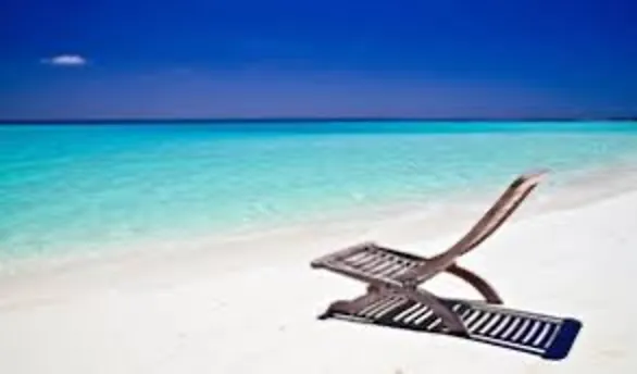 Beach lounge chair on white sand beside turquoise water